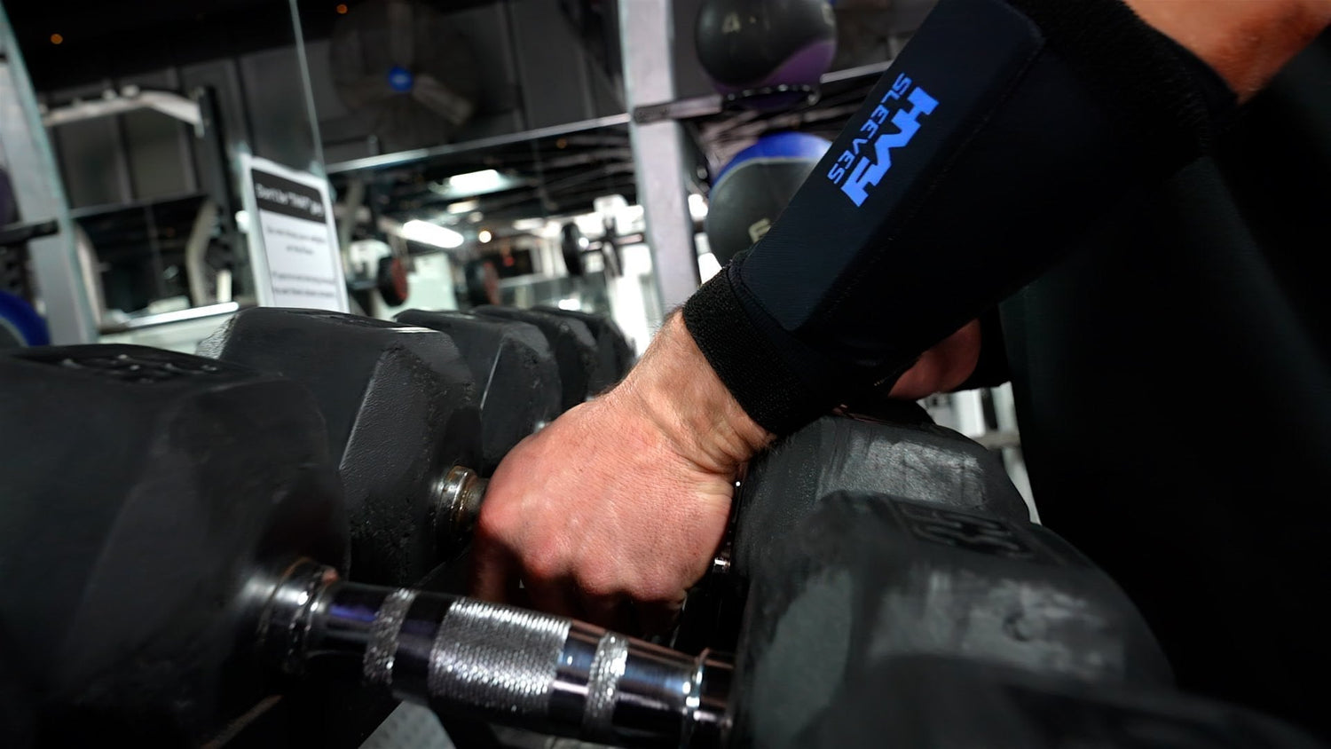 a man picking up heavy dumbbells in a gym while wearing HVY Sleeves on his arms