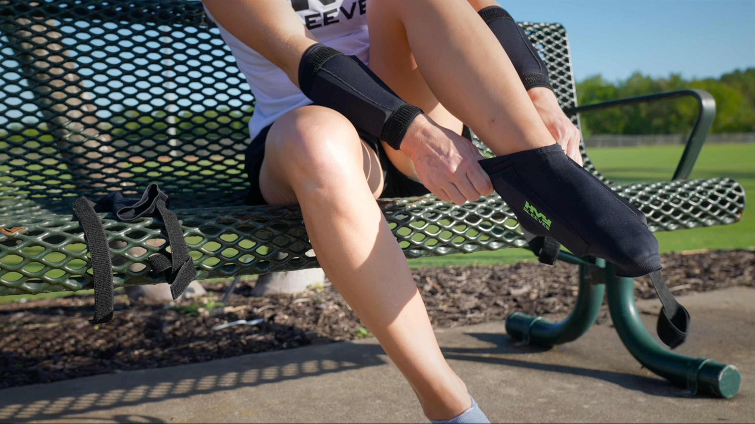 a woman putting on ankle weights on a bench in a park